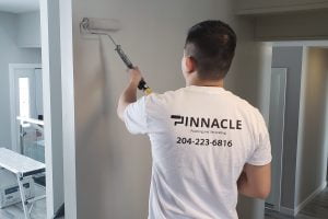 A painter in a white 'Pinnacle' branded shirt rolls paint on an interior wall.